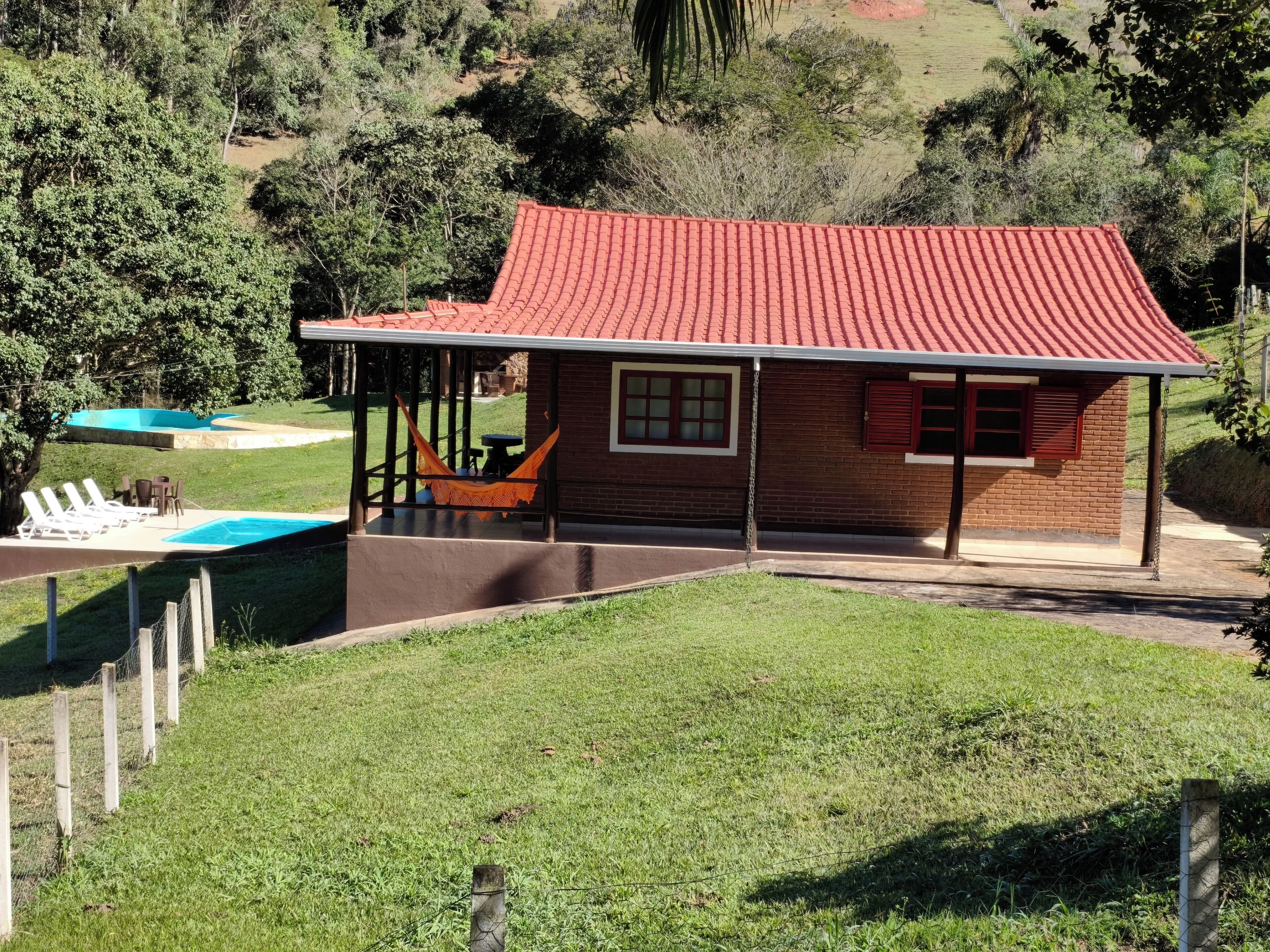Une maison avec un toit rouge, une piscine et un hamac.
