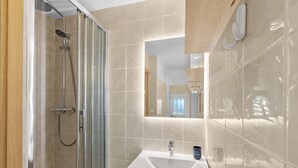 A modern bathroom with a glass shower enclosure, a white sink, and a mirror above it. - Apartment Horizon Bleu by Sur la mer (Les Issambres)