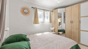 A bedroom with a bed, a wardrobe, a window with curtains, and a wall decoration. - Apartment Horizon Bleu by Sur la mer (Les Issambres)