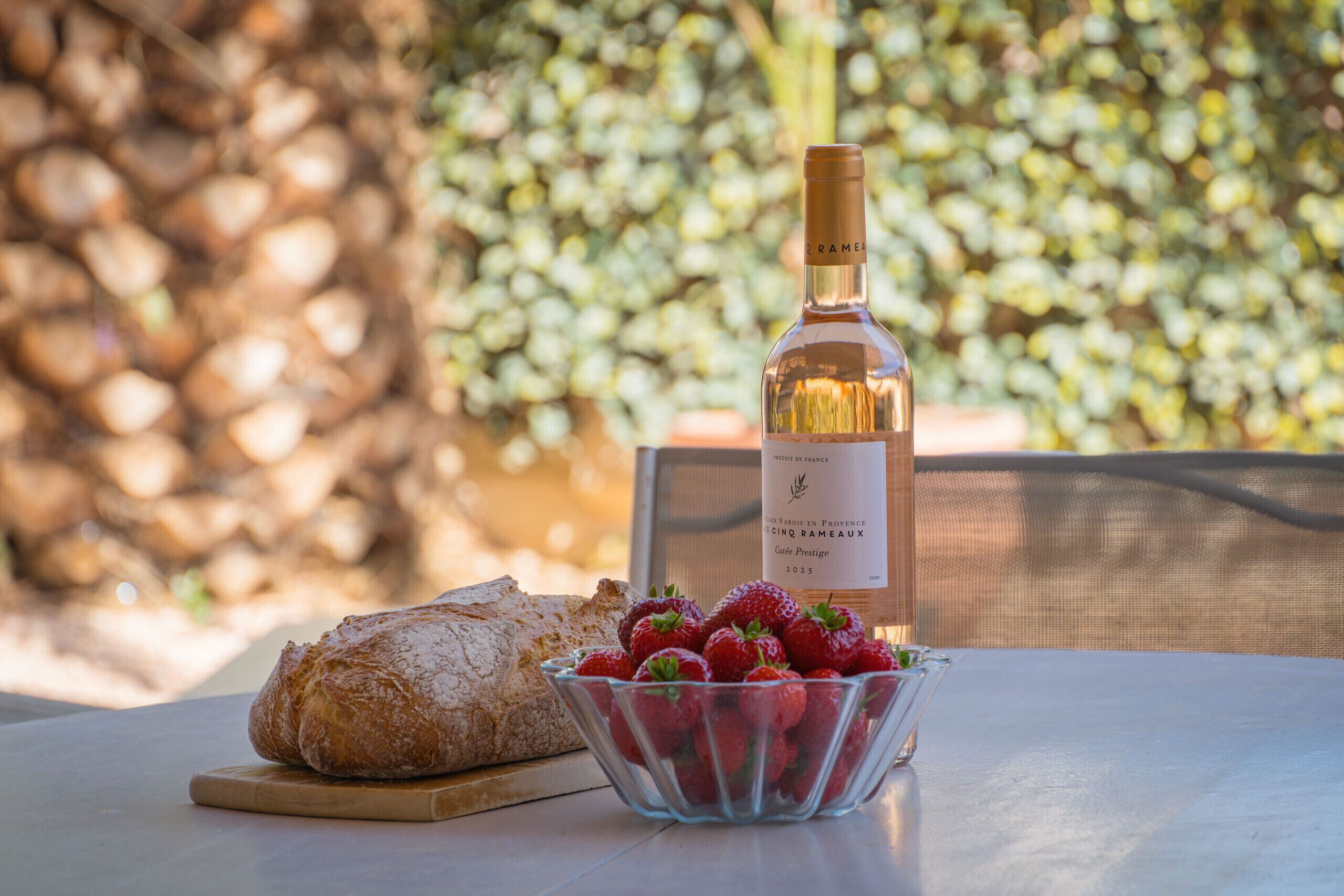 Una mesa con una botella de vino, un bol de fresas y una hogaza de pan.