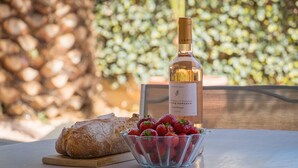 A table with a bottle of wine, a bowl of strawberries, and a loaf of bread. - Apartment Horizon Bleu by Sur la mer (Les Issambres)