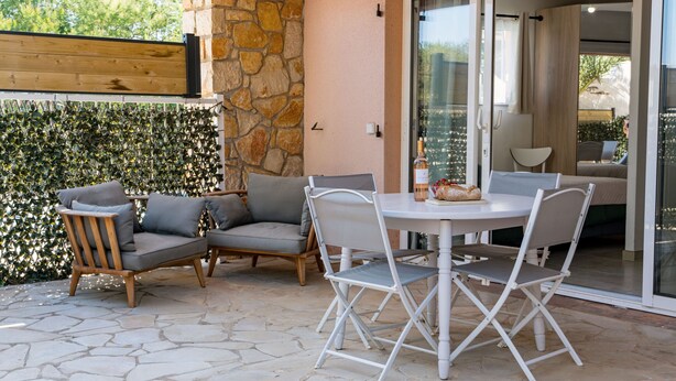 A patio area with stone flooring, a round table with chairs, and a stone wall with greenery. - Apartment Horizon Bleu by Sur la mer (Les Issambres)