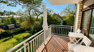 Ein Balkon mit weißer Reling, Tisch und Stühlen mit Blick auf eine grüne Rasenfläche und angrenzende Häuser.