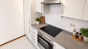 Una cocina moderna con armarios blancos, una campana extractora de acero inoxidable, una placa de inducción negra y un horno empotrado.