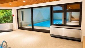 Un área de piscina interior moderna con paredes de vidrio, techo de madera y suelo de baldosas.