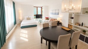 Habitación de hotel moderna con cama, televisor, zona de comedor y vistas al exterior.