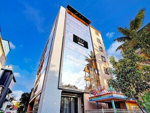 A modern hotel with a reflective glass facade, a prominent 'Collection' sign, and a traditional decorative structure with statues. - Classic With Balcony Bangalore Inn (Bengaluru)