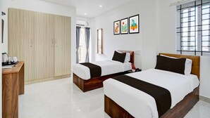 Une chambre d’hôtel avec deux lits, une armoire, un bureau et une fenêtre avec des stores.