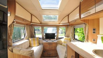 A compact RV interior with a central bed, a small kitchenette, and a skylight.
