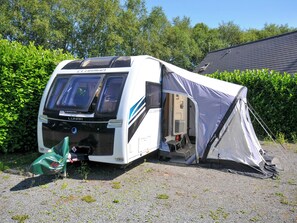 Een Clubman camperbus met een tent er naast, geparkeerd op een grindpad met groen op de achtergrond.
