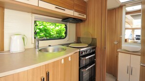 A compact kitchen with a window, sink, stove, and cabinets. - Rod and Rest (Chulmleigh)