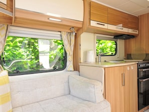 A compact RV interior with a kitchenette, a seating area, and a window with a view of greenery.