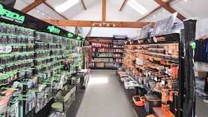 A store with shelves stocked with fishing tackle and accessories, wooden beams on the ceiling, and a clear aisle. - Rod and Rest (Chulmleigh)