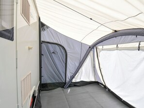 Interior de una caravana con toldo que incluye una zona de dormitorio, una ventana y una puerta.