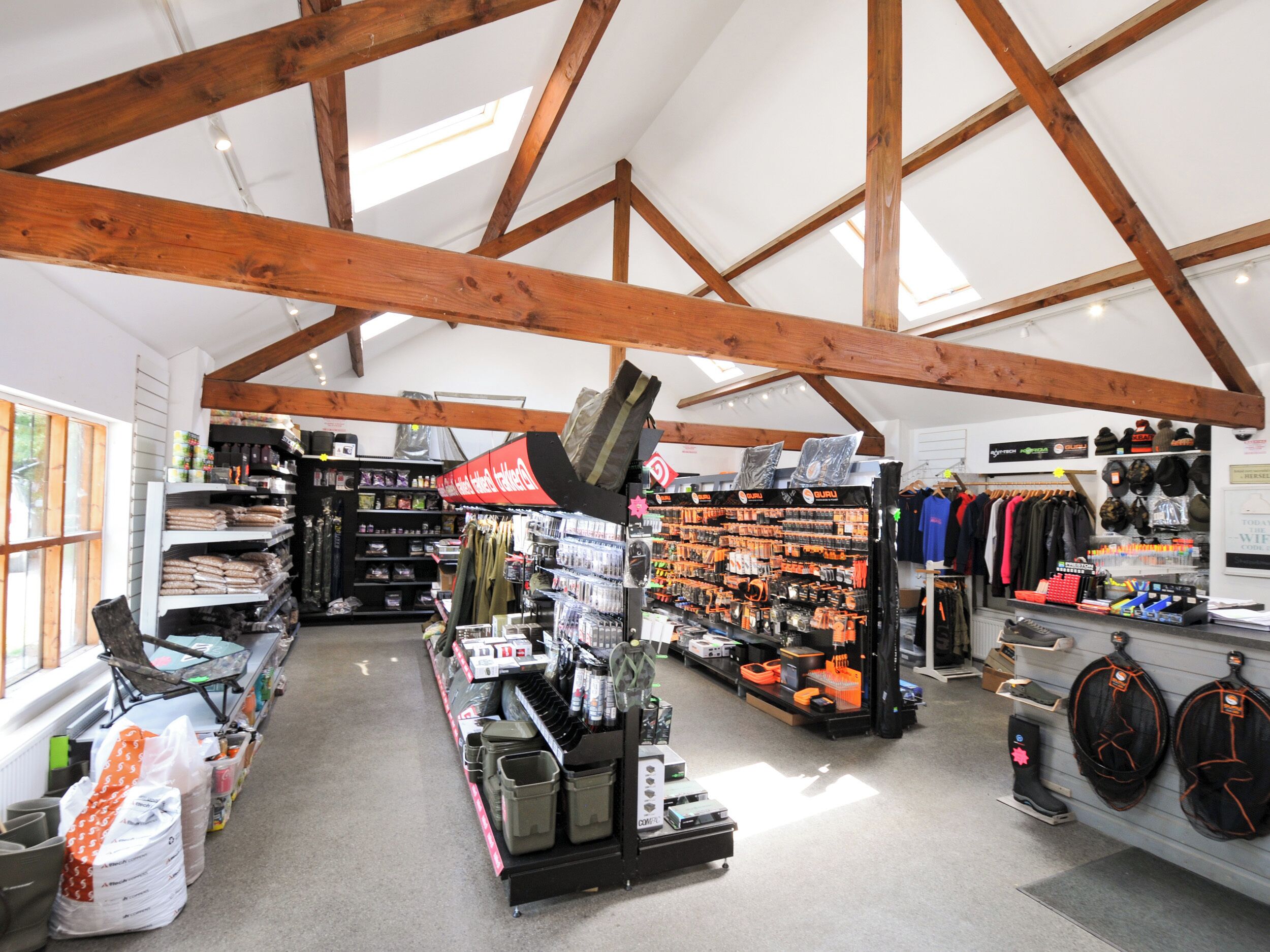 Ein geräumiger Laden mit hohen Decken und Holzbalken, mit Regalen voller verschiedener Produkte, darunter Kleidung und Accessoires.