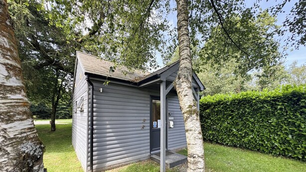 A small, single-story building with a dark exterior, a door, and a small porch area. - Rod and Rest (Chulmleigh)