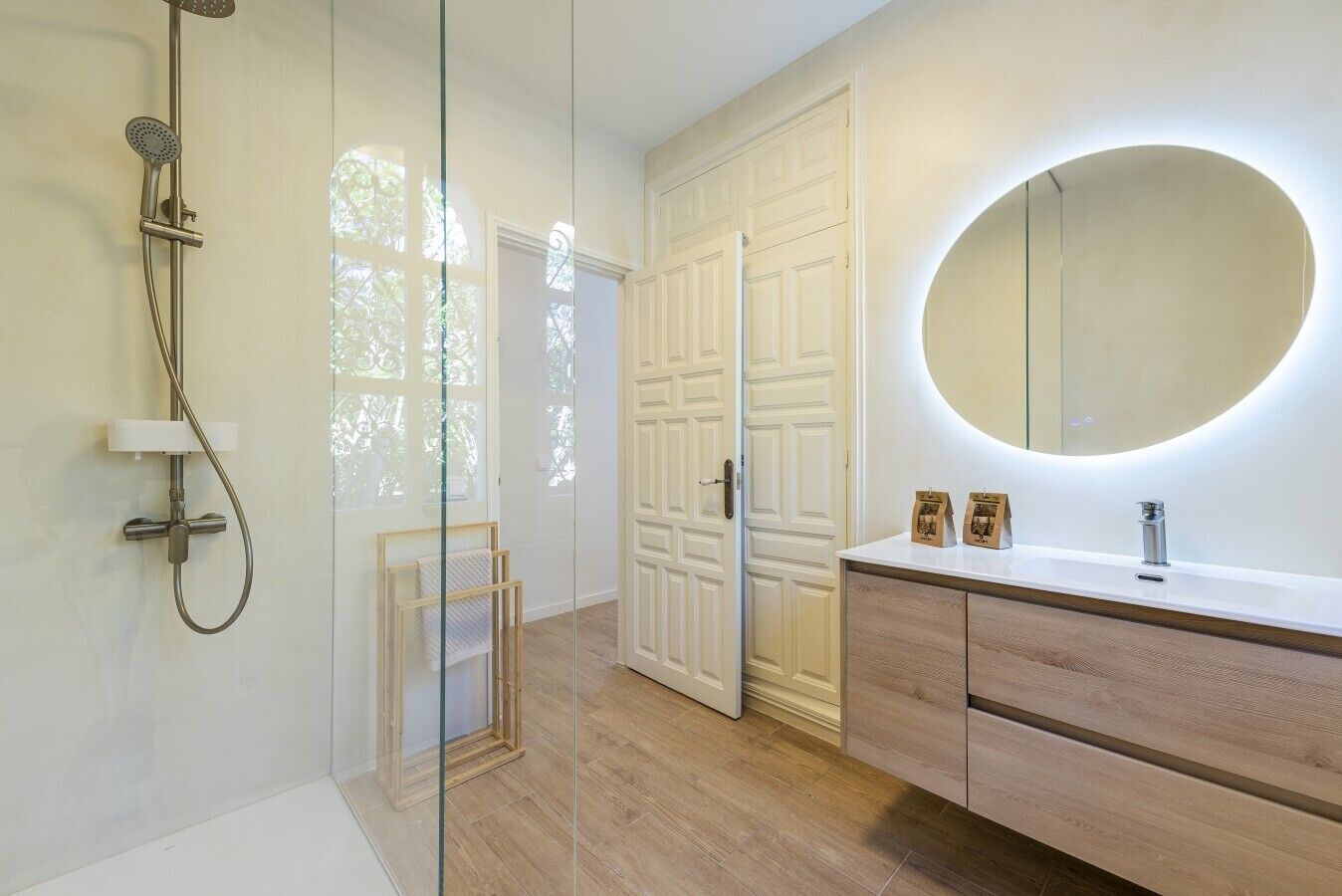 A modern bathroom with a glass shower enclosure, wooden vanity, and a large mirror.