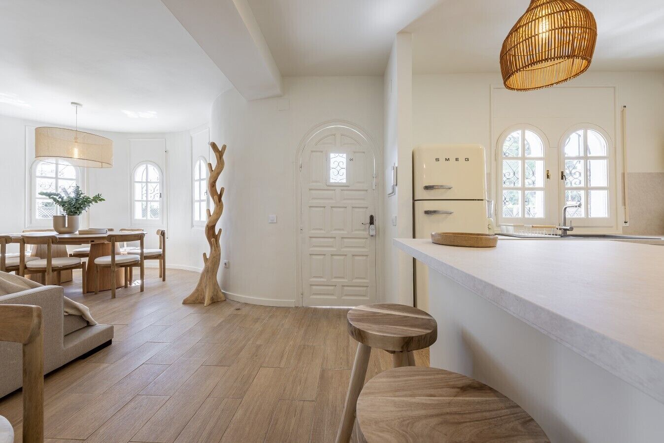 A modern kitchen with white cabinets, a wooden dining table, and a unique tree-shaped floor sculpture.