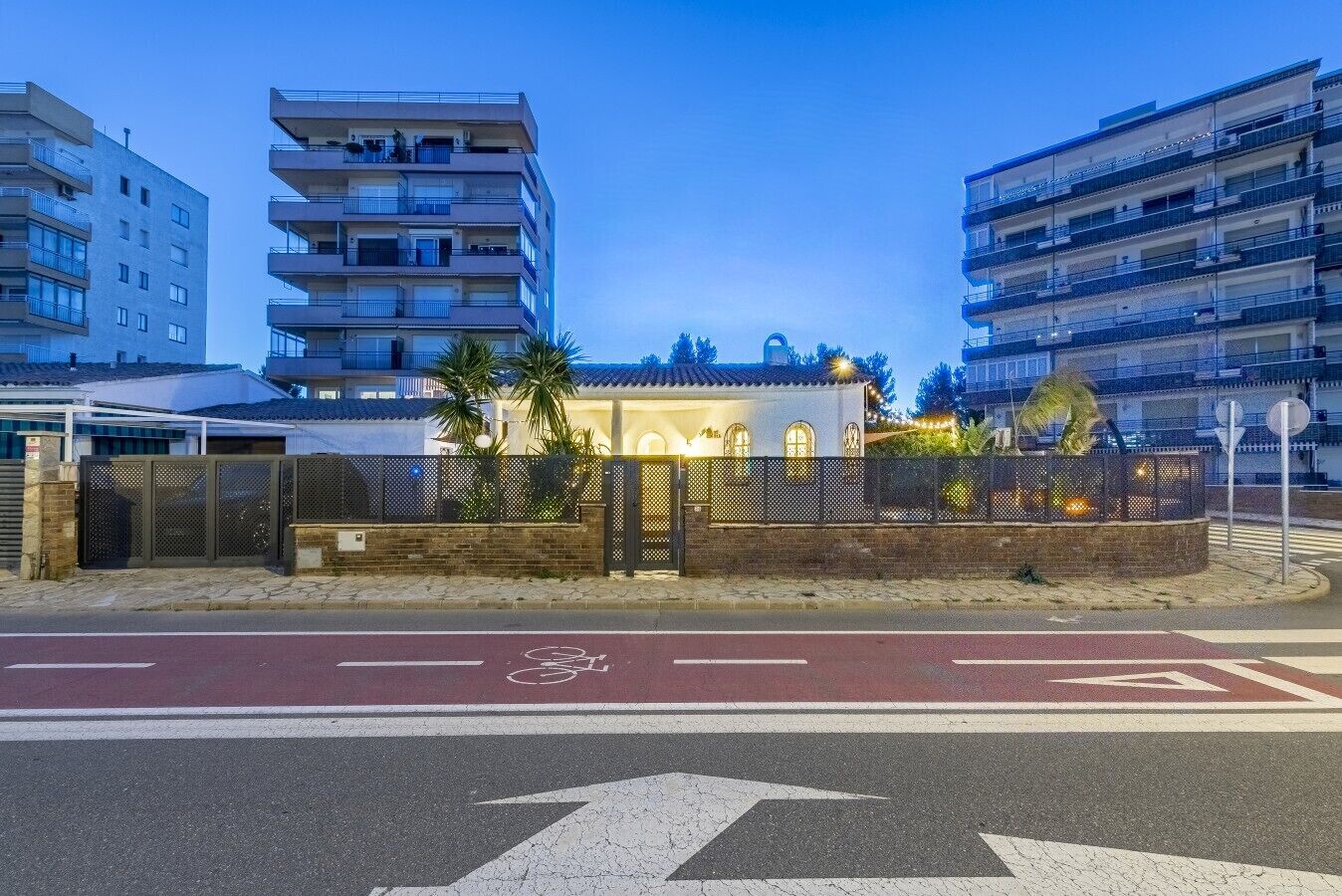 A multi-story residential building with balconies, a gated entrance, and a bicycle lane.