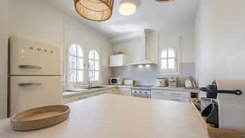 Cocina con electrodomésticos blancos, una isla grande y una lámpara colgante.