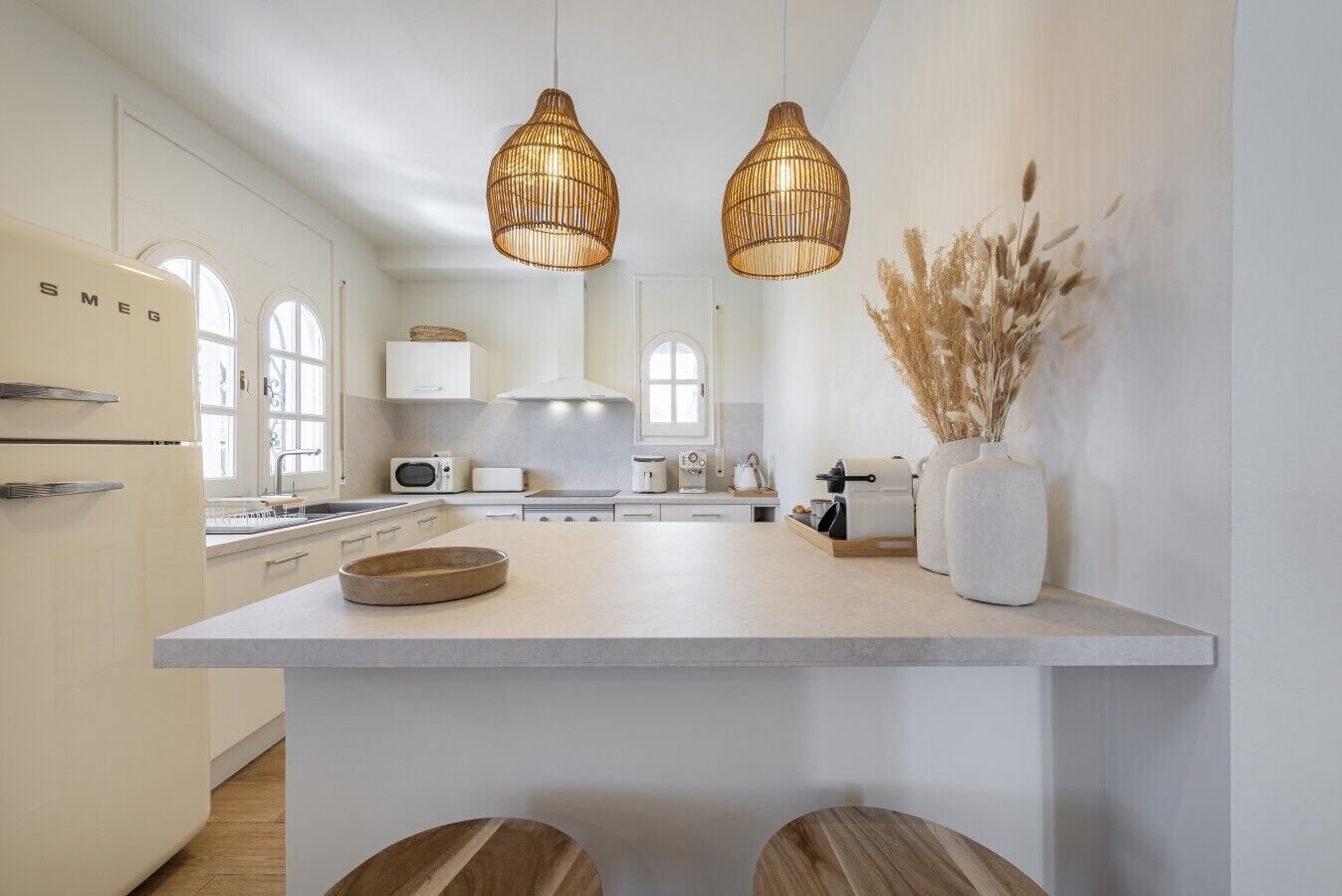 A modern kitchen with white cabinetry, a central island, and two hanging wicker pendant lights.