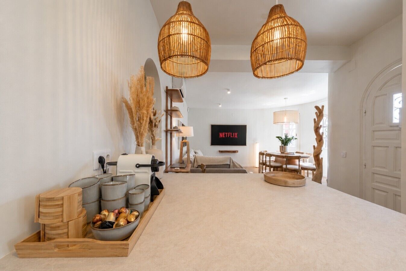 A modern living room with a large TV, two hanging wicker lamps, a wooden coffee table with bowls, and a sofa.