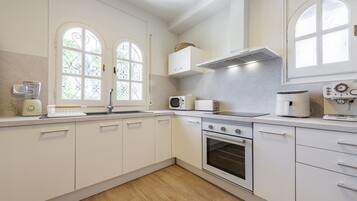 Une cuisine moderne avec des meubles blancs, un four encastré, un four à micro-ondes et une machine à café.