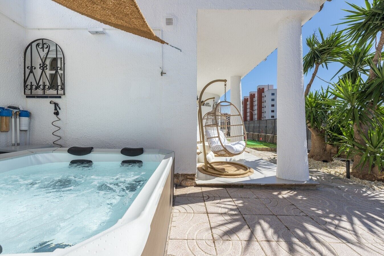 Un bain à remous avec un fauteuil suspendu, une fenêtre ornée d’une grille décorative et un mur blanc.