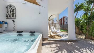 Un bain à remous avec un fauteuil suspendu, une fenêtre ornée d’une grille décorative et un mur blanc.