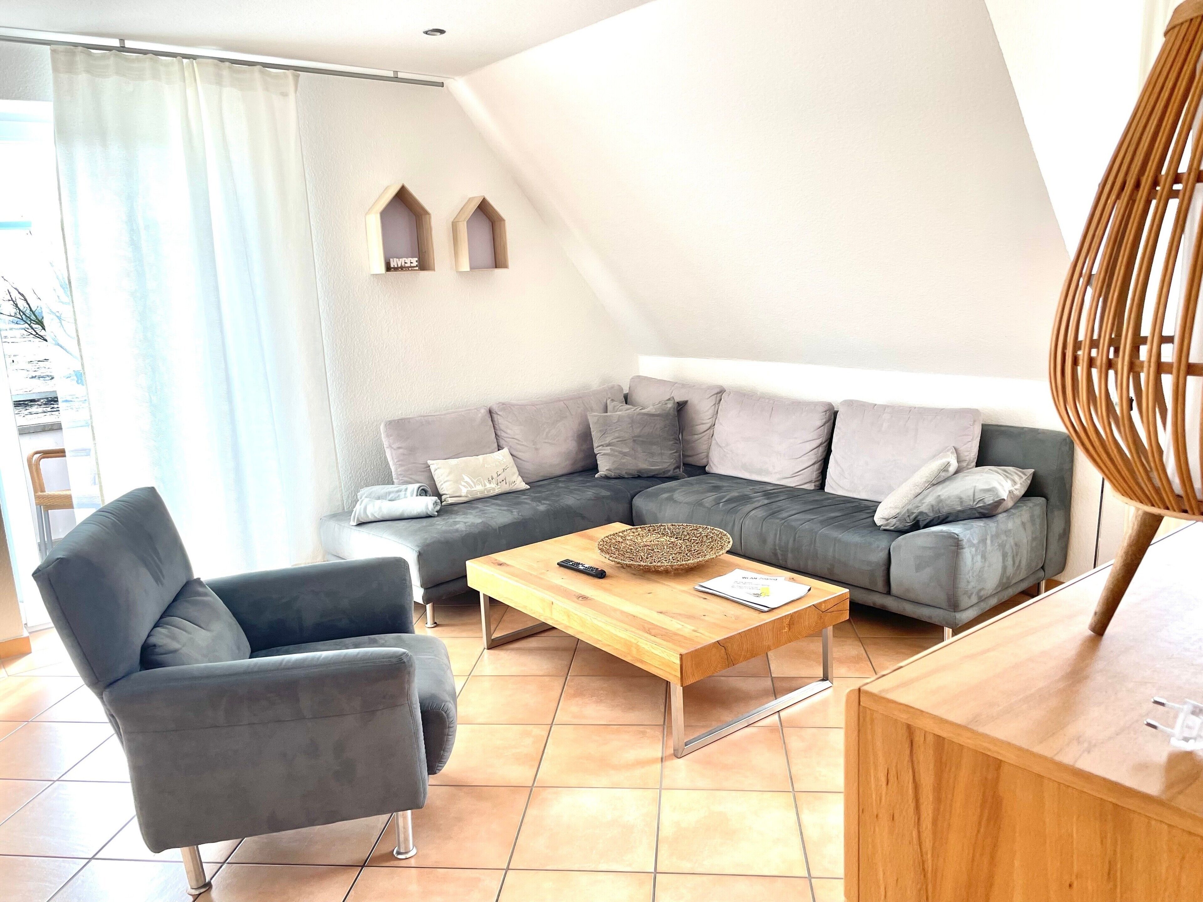 A modern living room with a grey sectional sofa, a wooden coffee table, a grey armchair, and a wicker bowl.