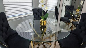 Een ronde glazen tafel met een gouden voet, omringd door zwarte stoelen met goudkleurige knopen.