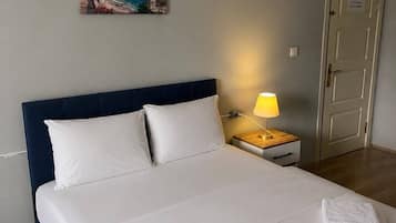 Una habitación de hotel con cama, mesita de noche, lámpara, un cuadro y una puerta.