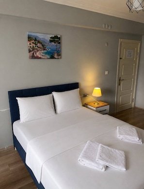 Una habitación de hotel con cama, mesita de noche, lámpara, un cuadro y una puerta.