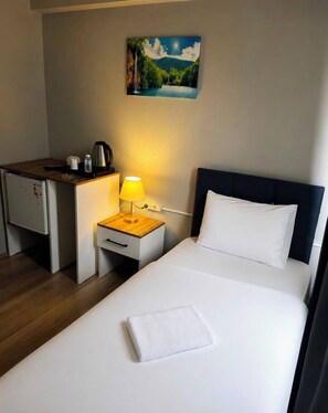 Habitación de hotel con cama, escritorio, mesita de noche, lámpara, un cuadro y cafetera.