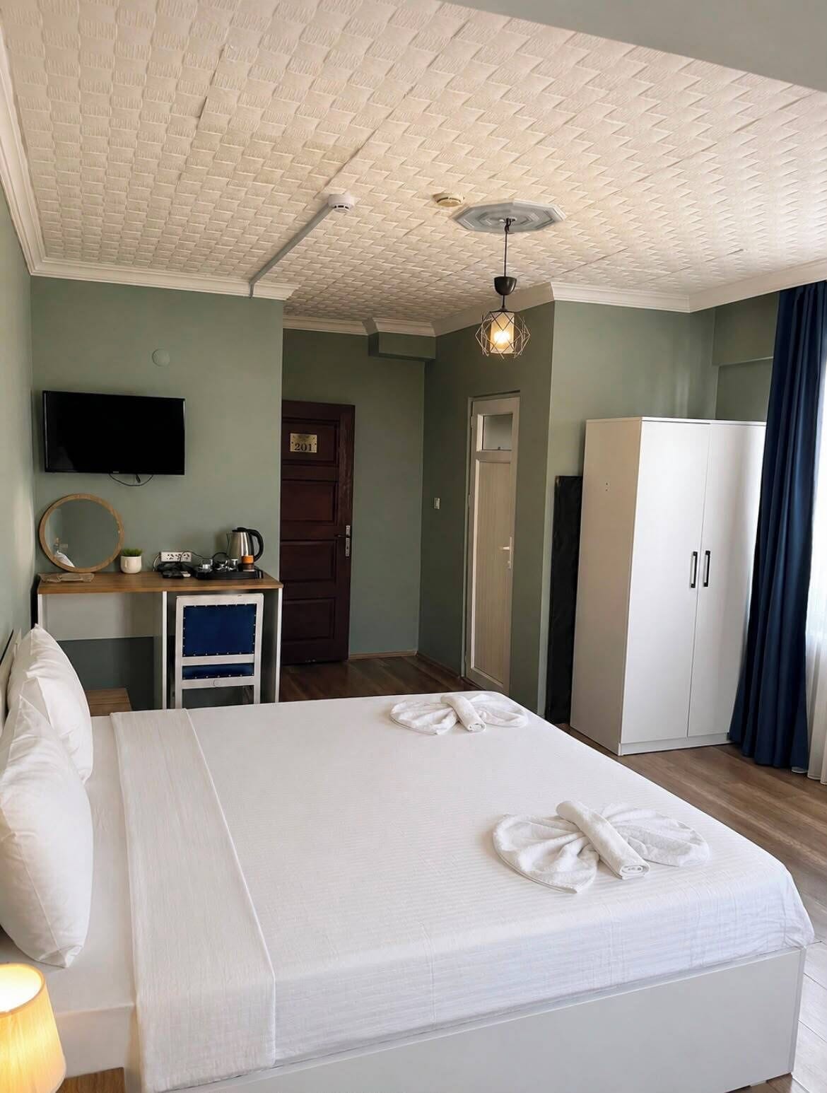 A hotel room with a bed, a desk, a wardrobe, a television, and a door.