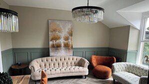 Ein Zimmer mit einer рарpensofa, zwei Sesseln, einem Holzboden im Fischgrätmuster, einem großen Gemälde und einer Chandelier.