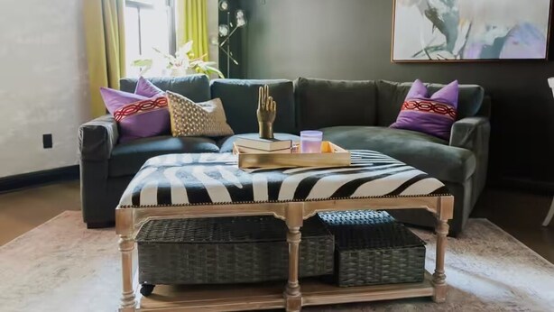 Un salon avec un canapé vert foncé, un pouf à rayures zébrées et un plateau contenant des livres et un verre.