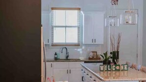 Une cuisine moderne avec des meubles blancs, un îlot central et un coin repas agrémenté de chaises à motifs.