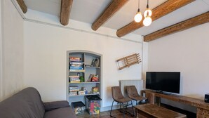 Ein Wohnzimmer mit einer Couch, zwei Sesseln, einem Holztisch, einem Fernseher und einem Bücherregal mit Gesellschaftsspielen.