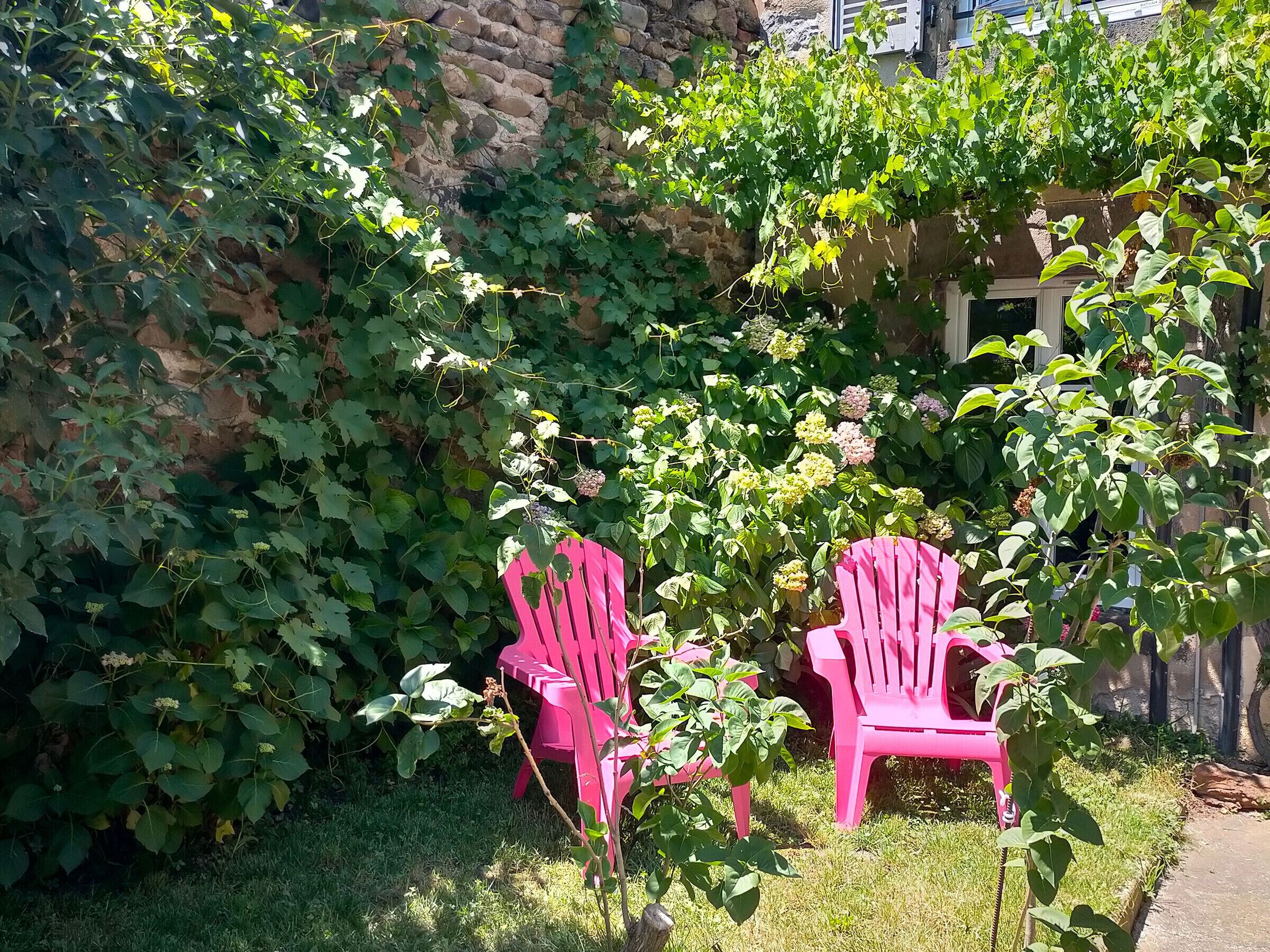 Two pink chairs in a garden with a stone wall and greenery.