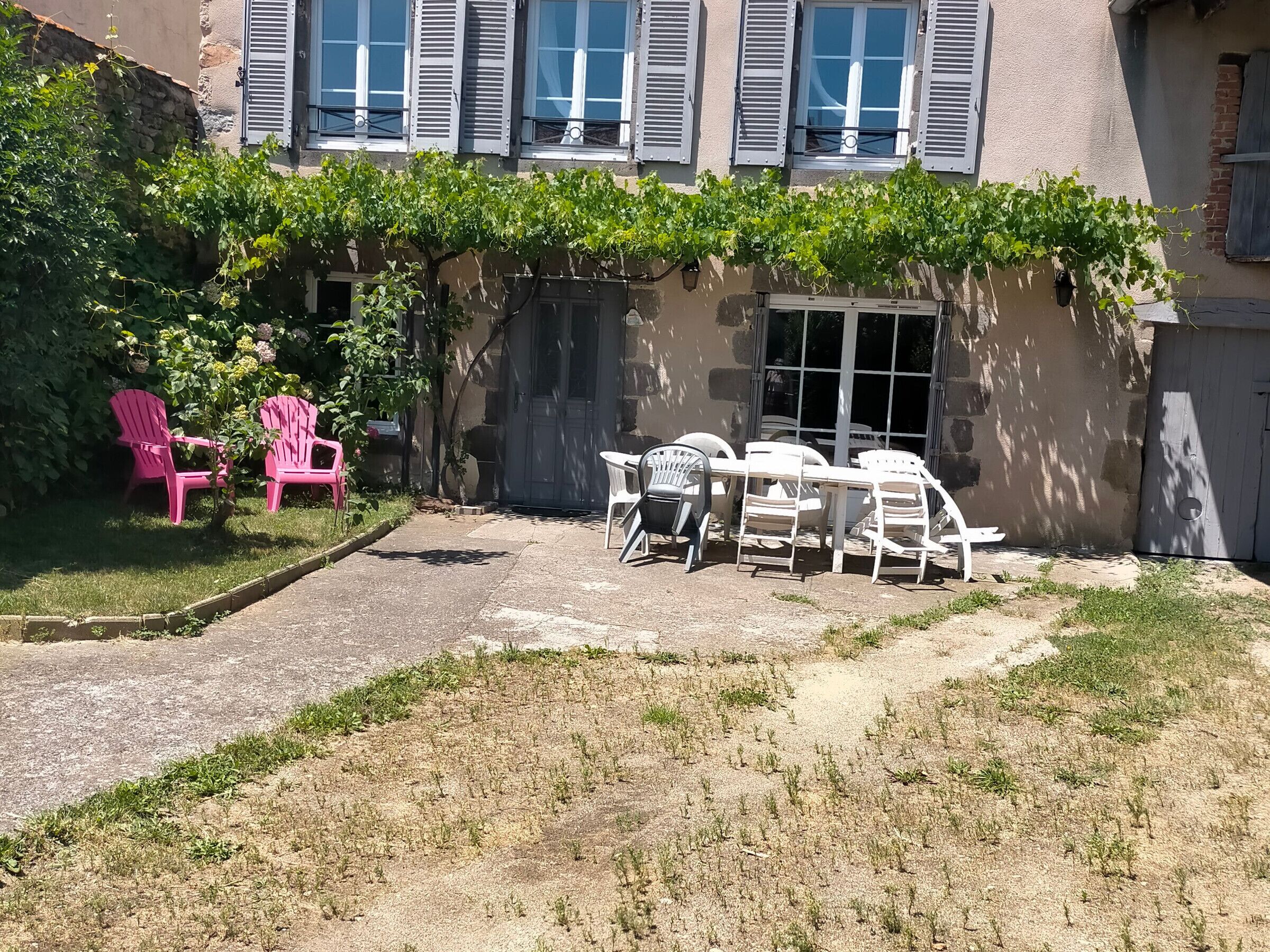 Eine Terrasse mit Gartenmöbeln, einer Steinmauer und einem Gebäude mit Fensterläden.