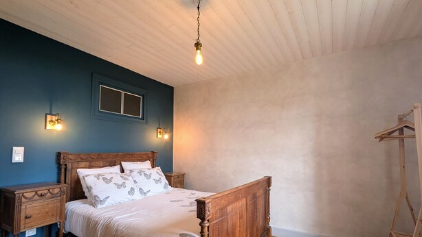 Ein Schlafzimmer mit einem hölzernen Bett, Nachttischen, einer Pendelleuchte und einer Holzleiter an der Wand.