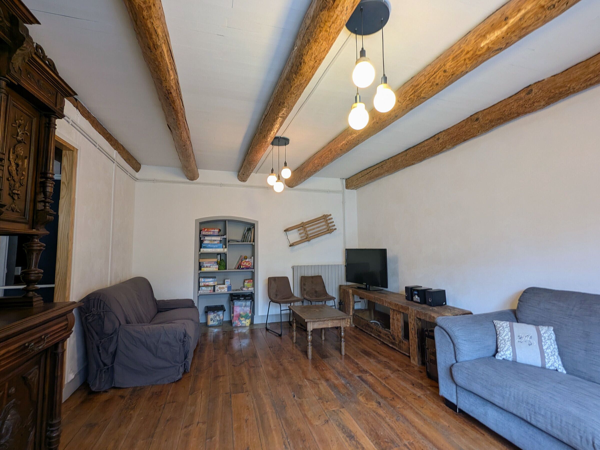 A living room with wooden beams, a bookshelf, a television, and two sofas.