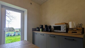 Eine Küche mit Holzausziehtisch, einer Mikrowelle, einer Kaffeemaschine und Blick auf eine Grünfläche.