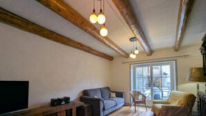 Ein Wohnzimmer mit Holzbalken, einem grauen Sofa, einem Korbstuhl, einem Holztisch und einem Fernseher.