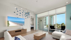 Ein modernes Wohnzimmer mit großem Fernseher, einer Couch, einem Couchtisch und einem Balkon mit Meerblick.