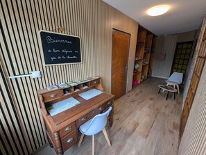A wooden desk with drawers and a white chair, a chalkboard with a welcome message, and a bookshelf with books and a globe. - Countryside cottage, pets welcome, lush area (Mélisey)