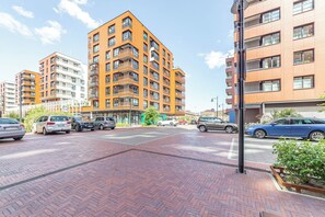 Un immeuble résidentiel à plusieurs étages doté de balcons, d’un espace de stationnement avec des voitures et d’un chemin piétonnier.