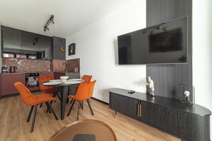 Een moderne keuken met een eethoek, een wandgemonteerde flatscreen-tv en een houten vloer.