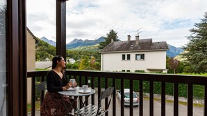 En balkong med ett bord och stolar, med utsikt över ett vitt hus och berg.